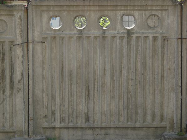 Concrete fence texture molded with a pattern of circles above vertical recessions, with large cracks and stains. The fence appears to be crumbling around the edges.